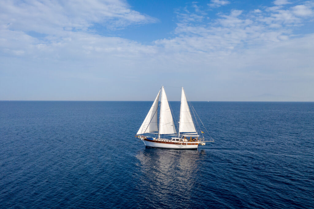 Sailing. Ship yacht, luxury boat with white sails in the open sea. Wooden vintage sailboat, cloudy blue sky background. Aegean sea Greece